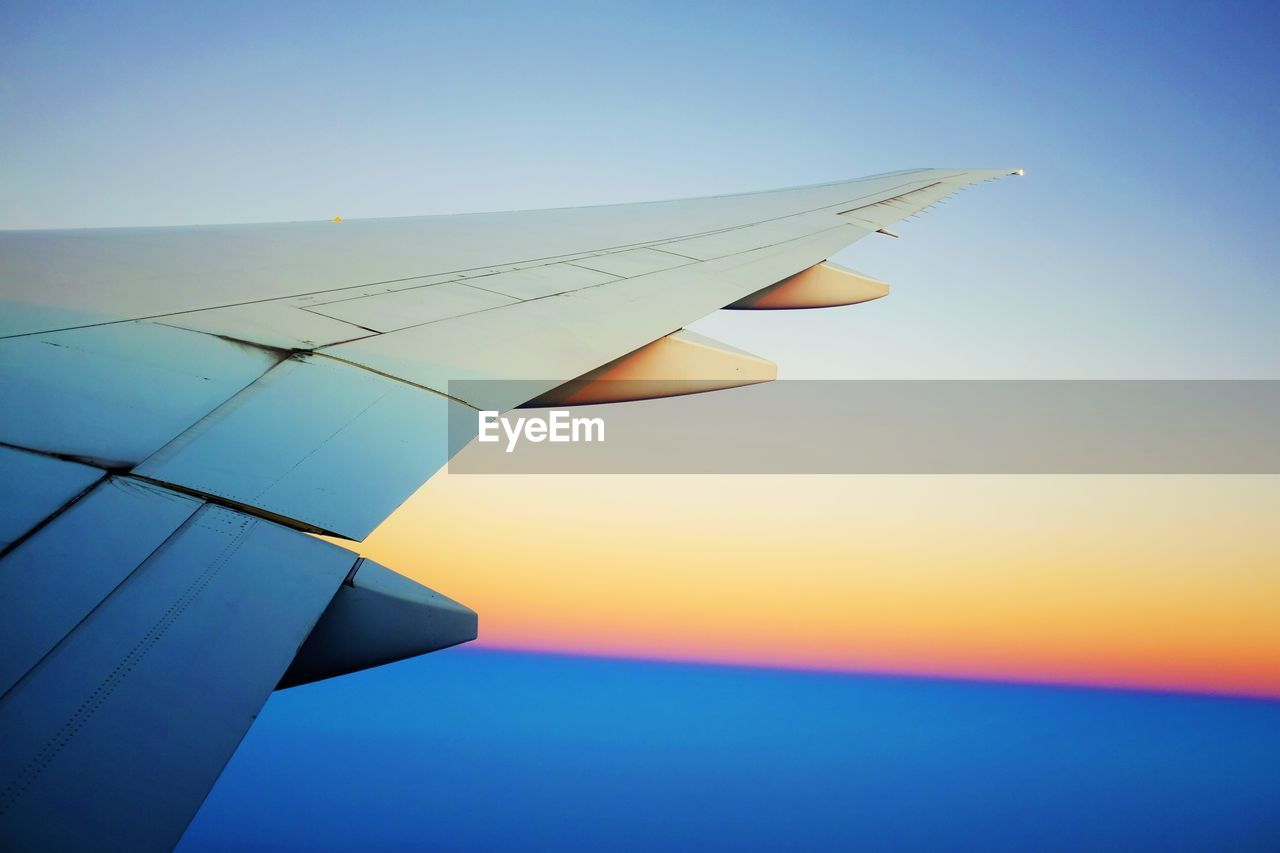 Cropped image of aircraft wing against sky during sunset 