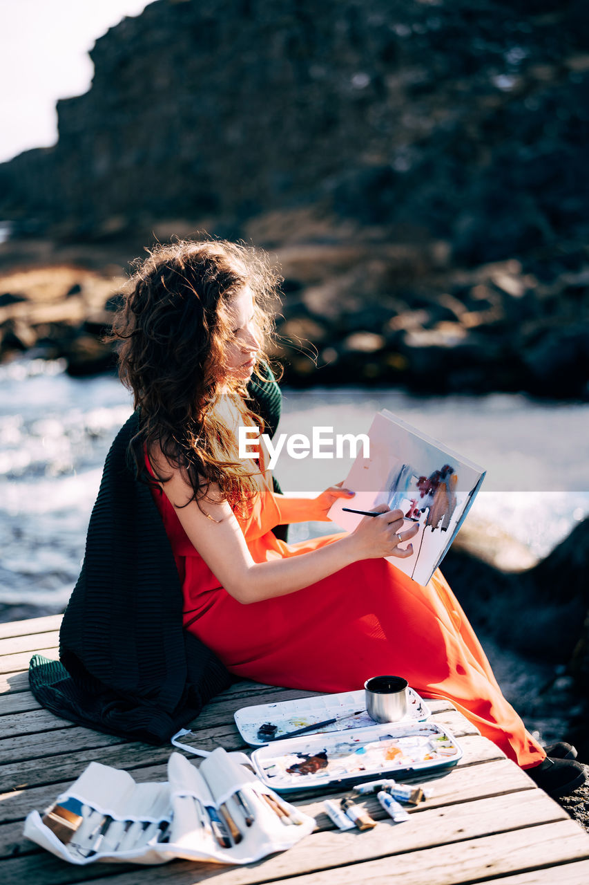 MIDSECTION OF WOMAN SITTING ON ROCK