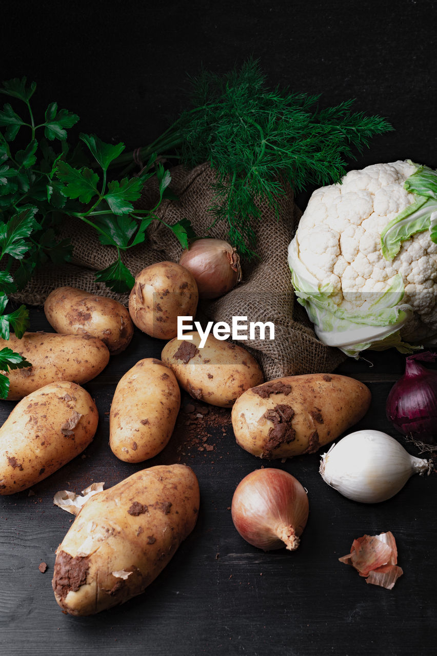 Potatoes, cauliflower, onions and herbs on dark table