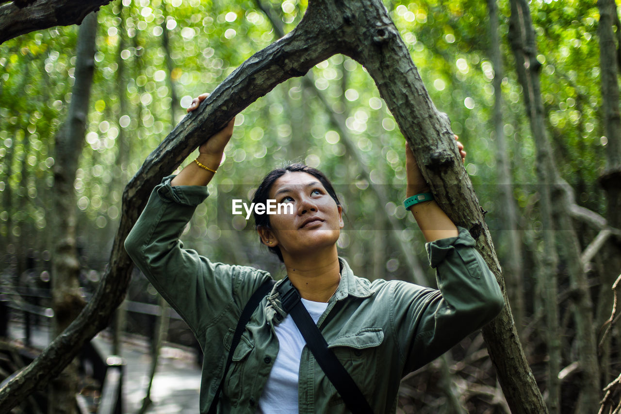 Smiling woman looking up while standing amidst trees in forest