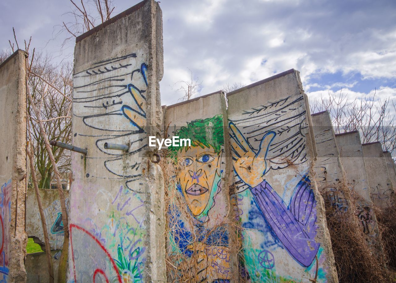 Low angle view of graffiti on berlin wall against cloudy sky