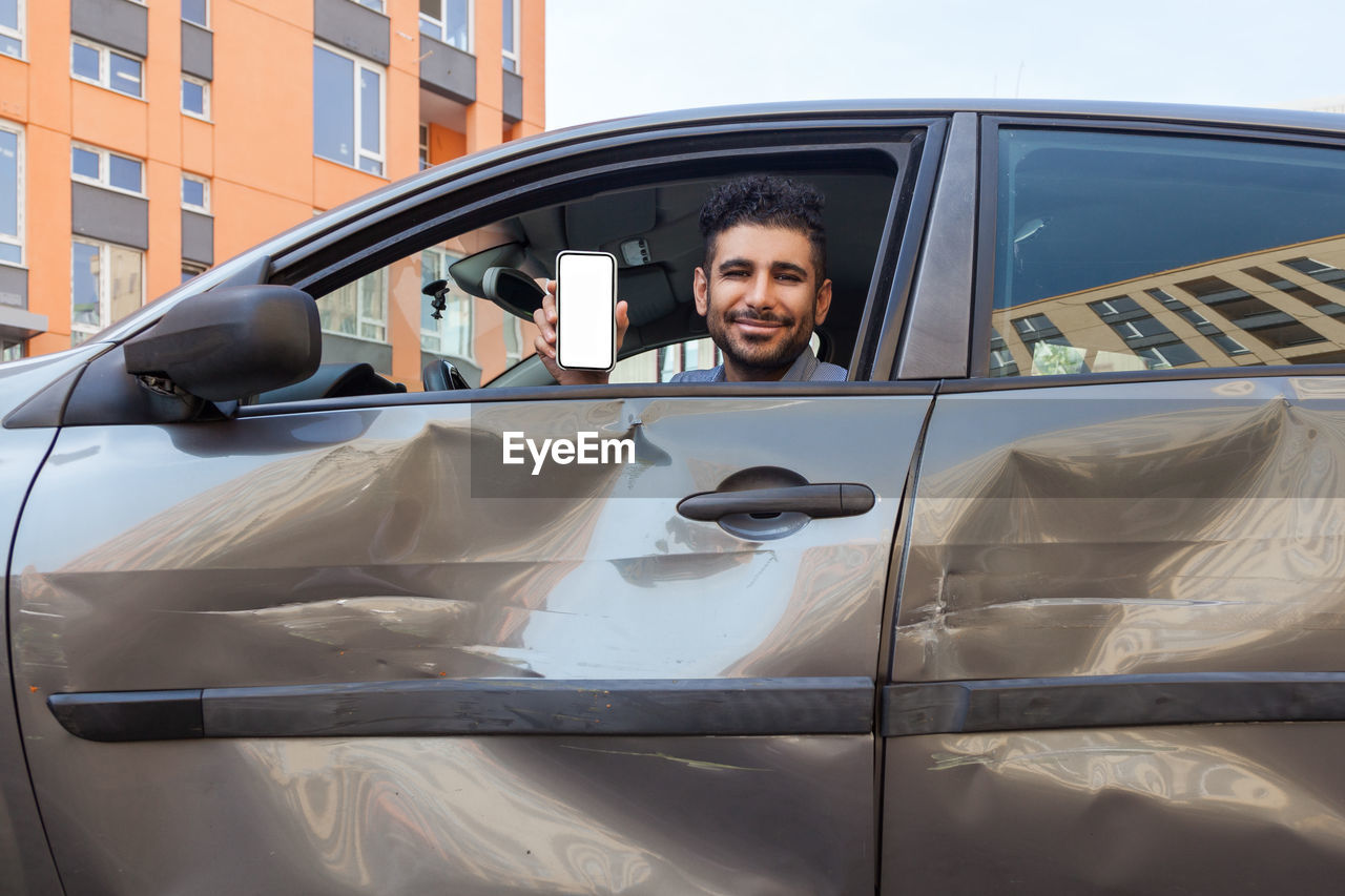 PORTRAIT OF SMILING YOUNG MAN ON CAR