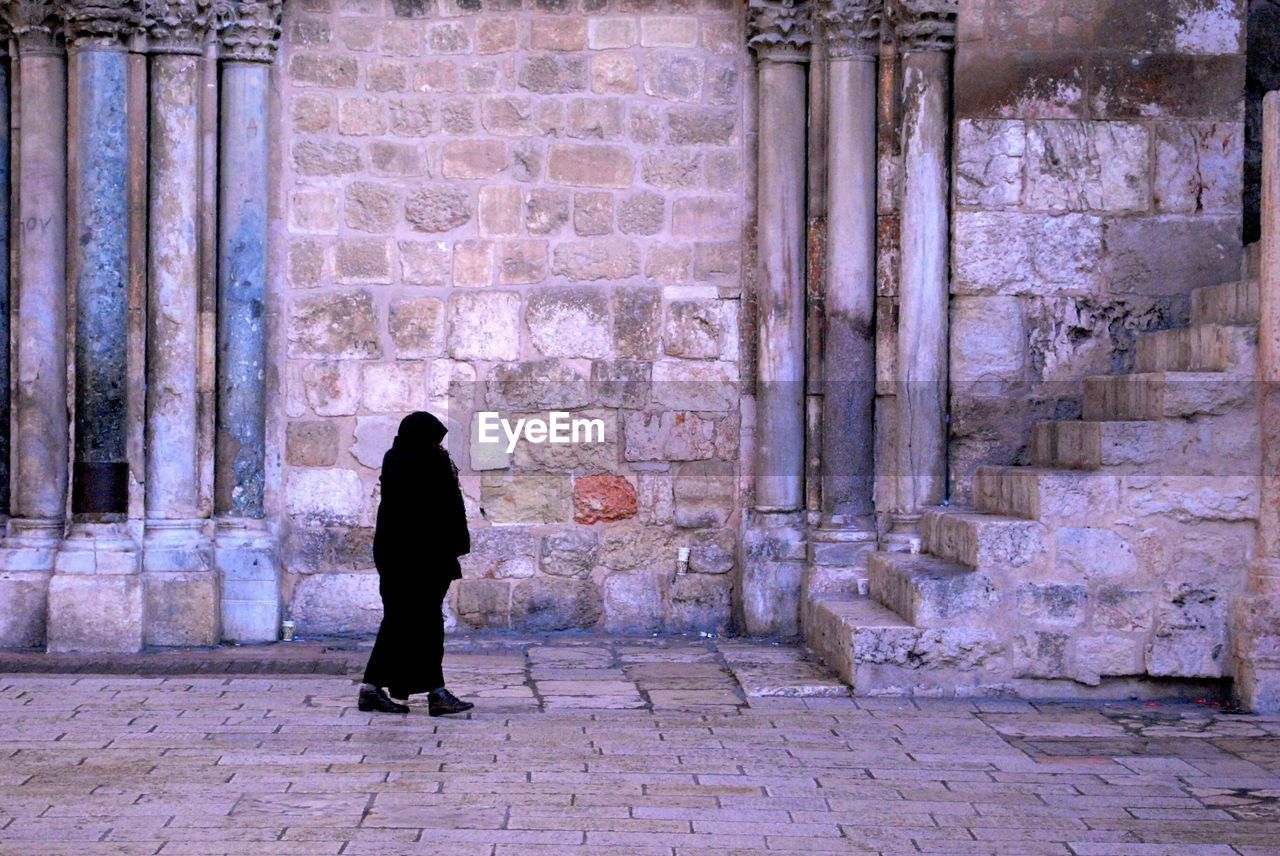 Woman in burka walking on street by old building