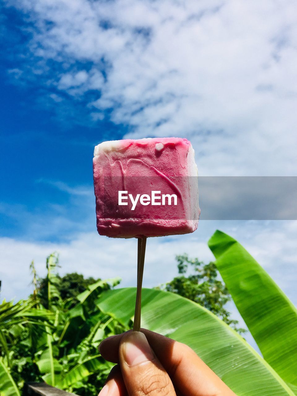 Close-up of hand holding ice cream against sky