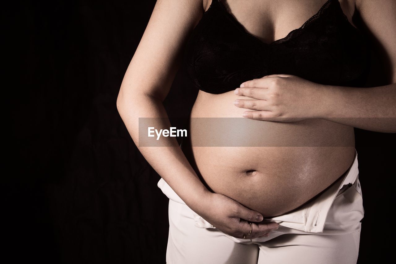 MIDSECTION OF WOMAN TOUCHING AGAINST BLACK BACKGROUND