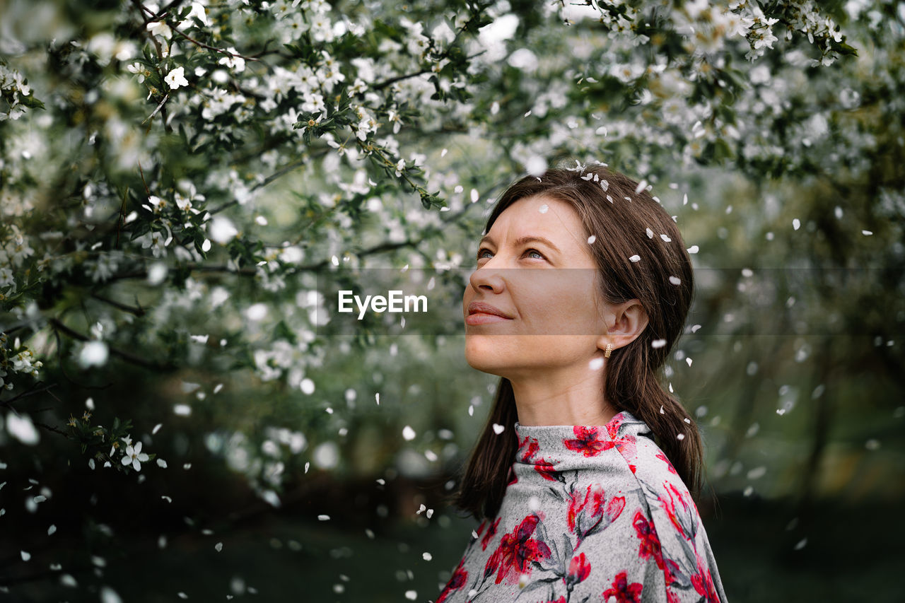 Portrait of a beautiful young woman looking away by blooming tree in spring