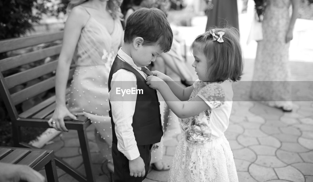 Cute sister adjusting brother tie with people in background during wedding