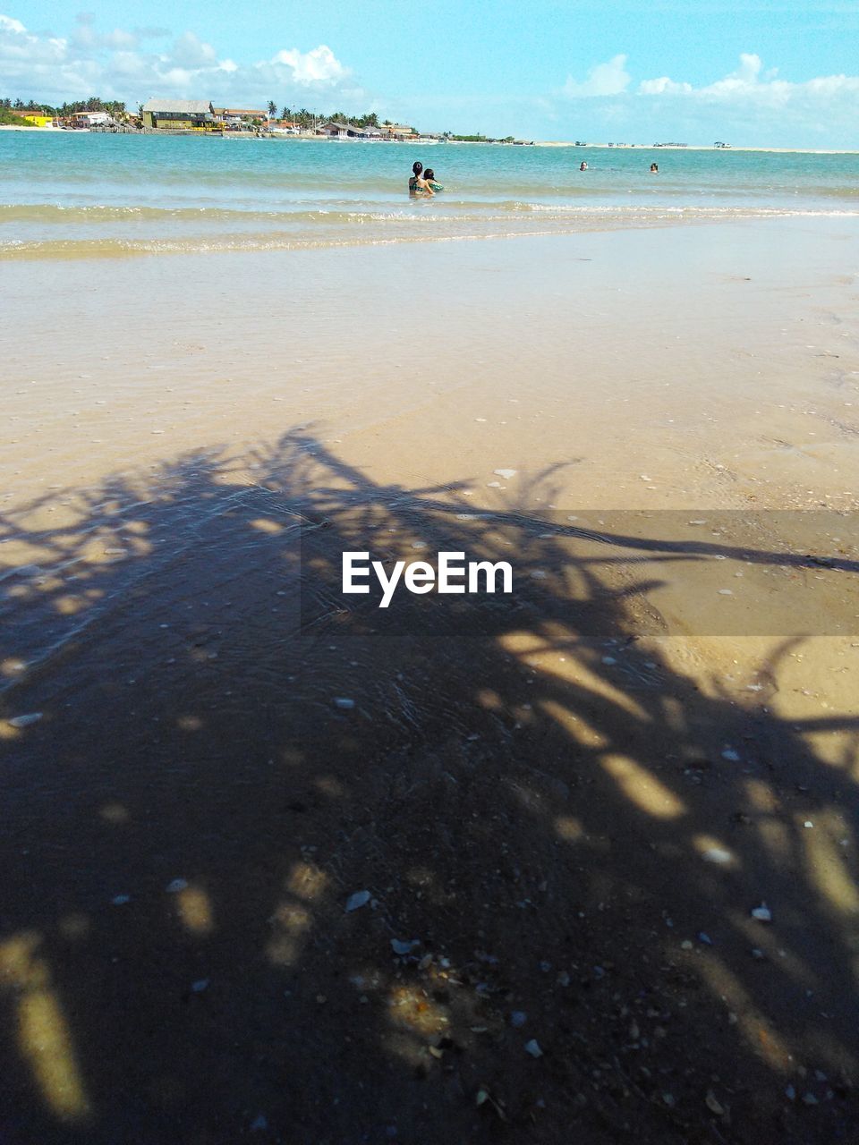 The shadow of a thatched beach hut leading to kids swimming in a river