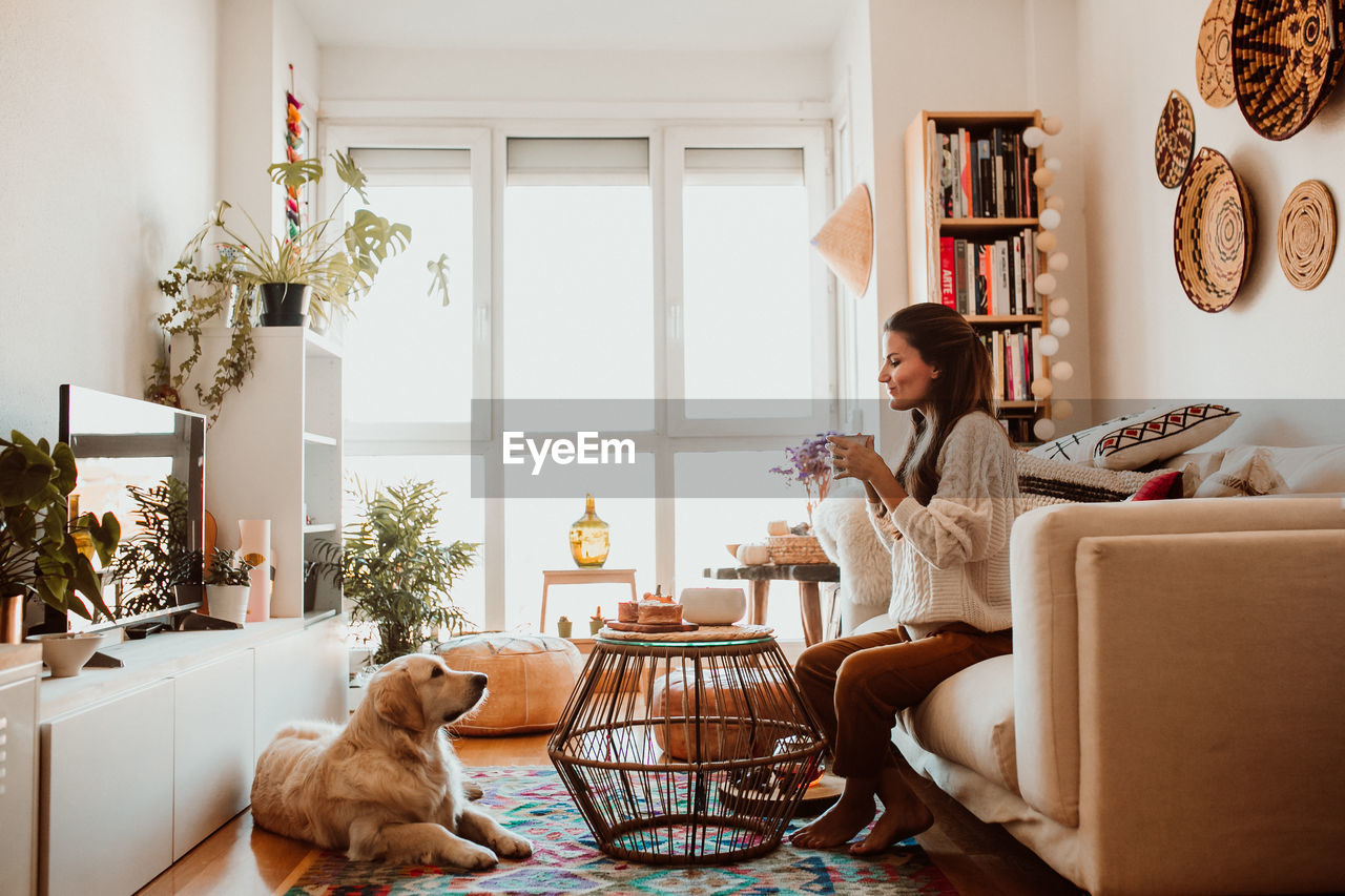 Side view of woman looking at dog while sitting on sofa