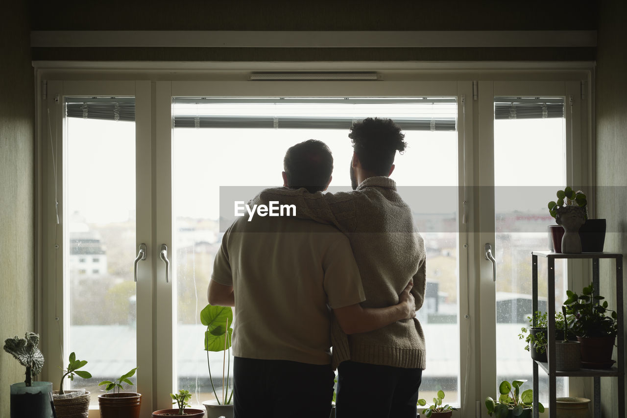 Homosexual couple standing with arms around and looking through window