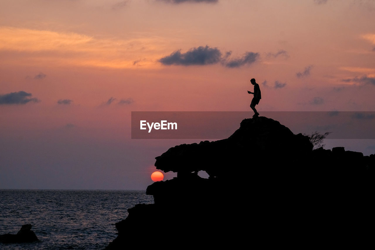 Silhouette rock in sea against sky during sunset