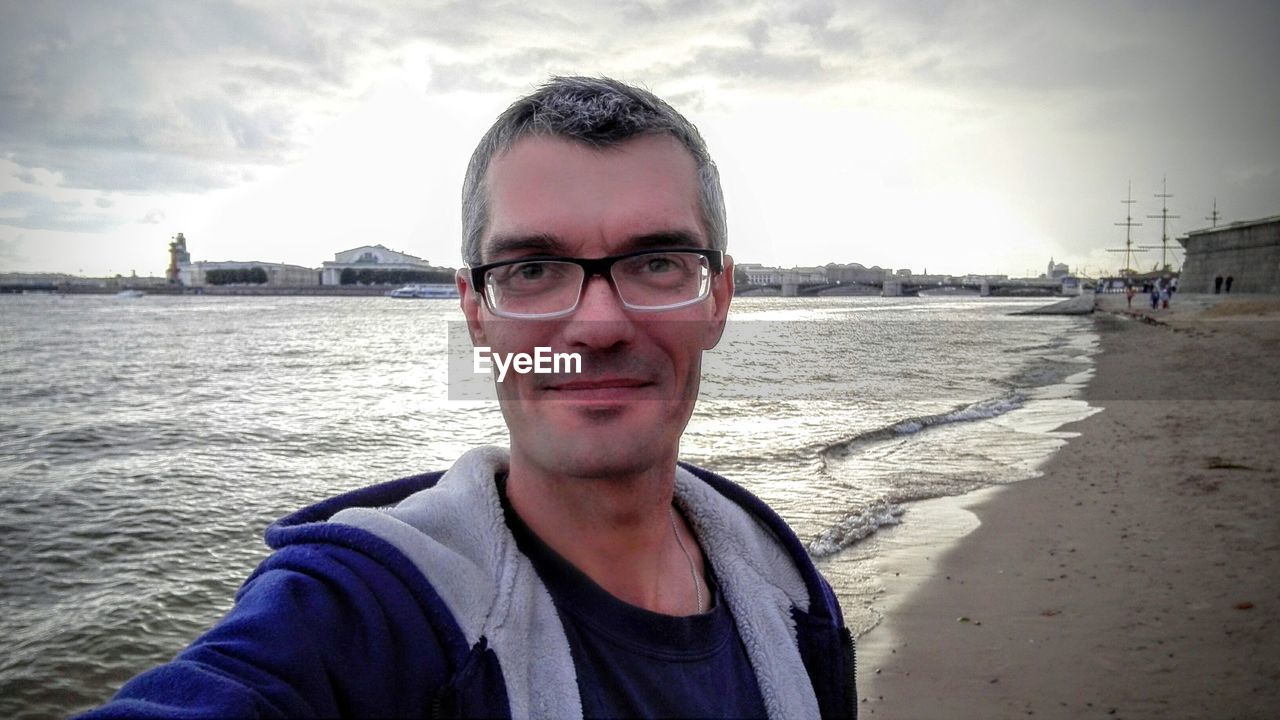 Portrait of mature man wearing eyeglasses while standing on shore at beach