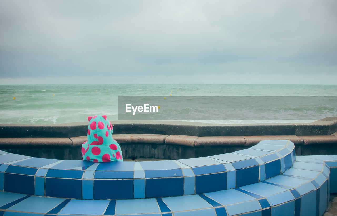 Little girl in a bathrobe sitting facing the sea