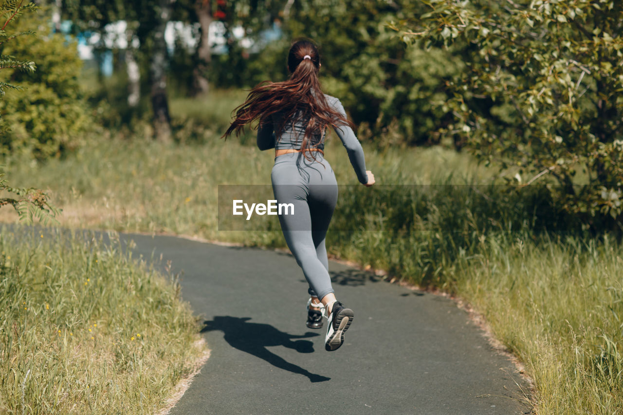 Rear view of woman running on road against trees