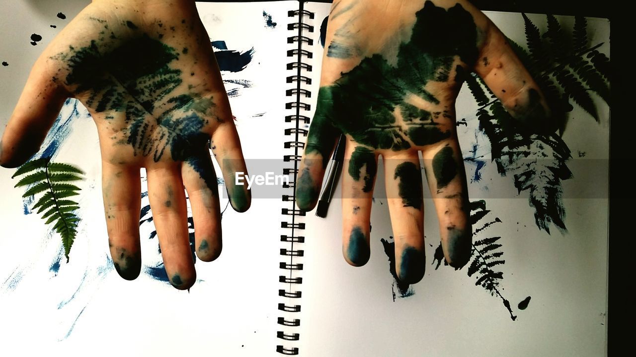 Cropped hands with green paint over book