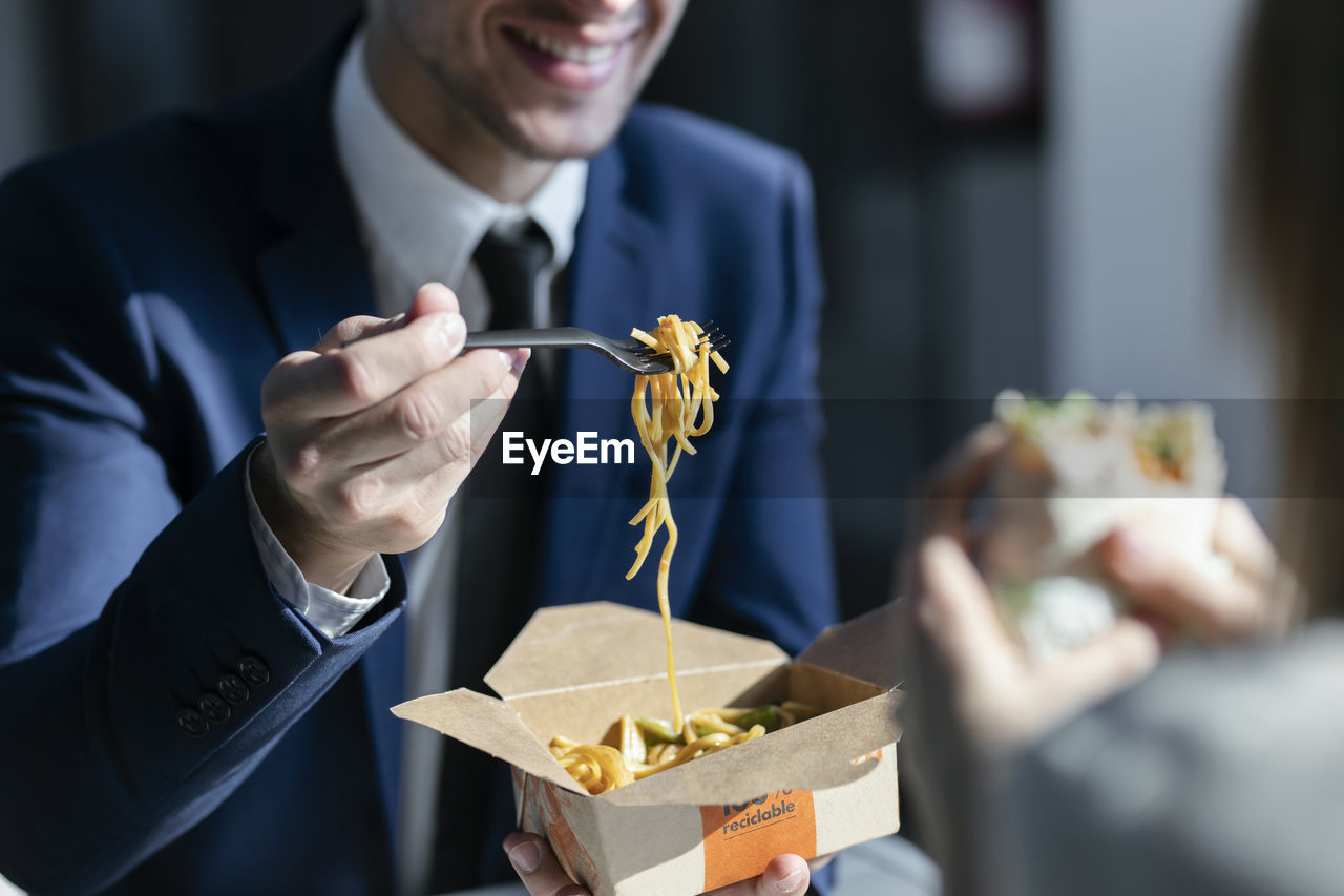 Businessman eating noodles while sitting with colleague in cafeteria at office