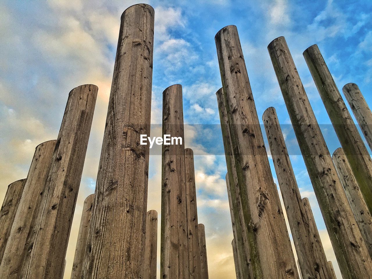 Low angle view of wooden posts against cloudy sky