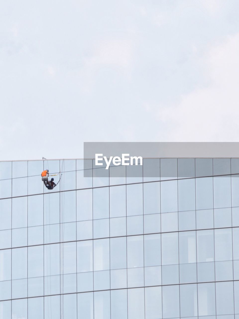 Low angle view of worker washing window on building against clear sky