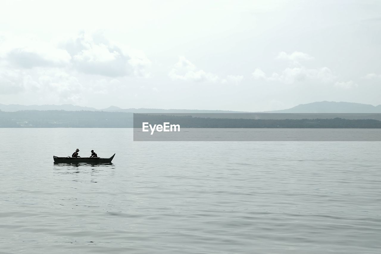 People traveling in boat at sea against sky