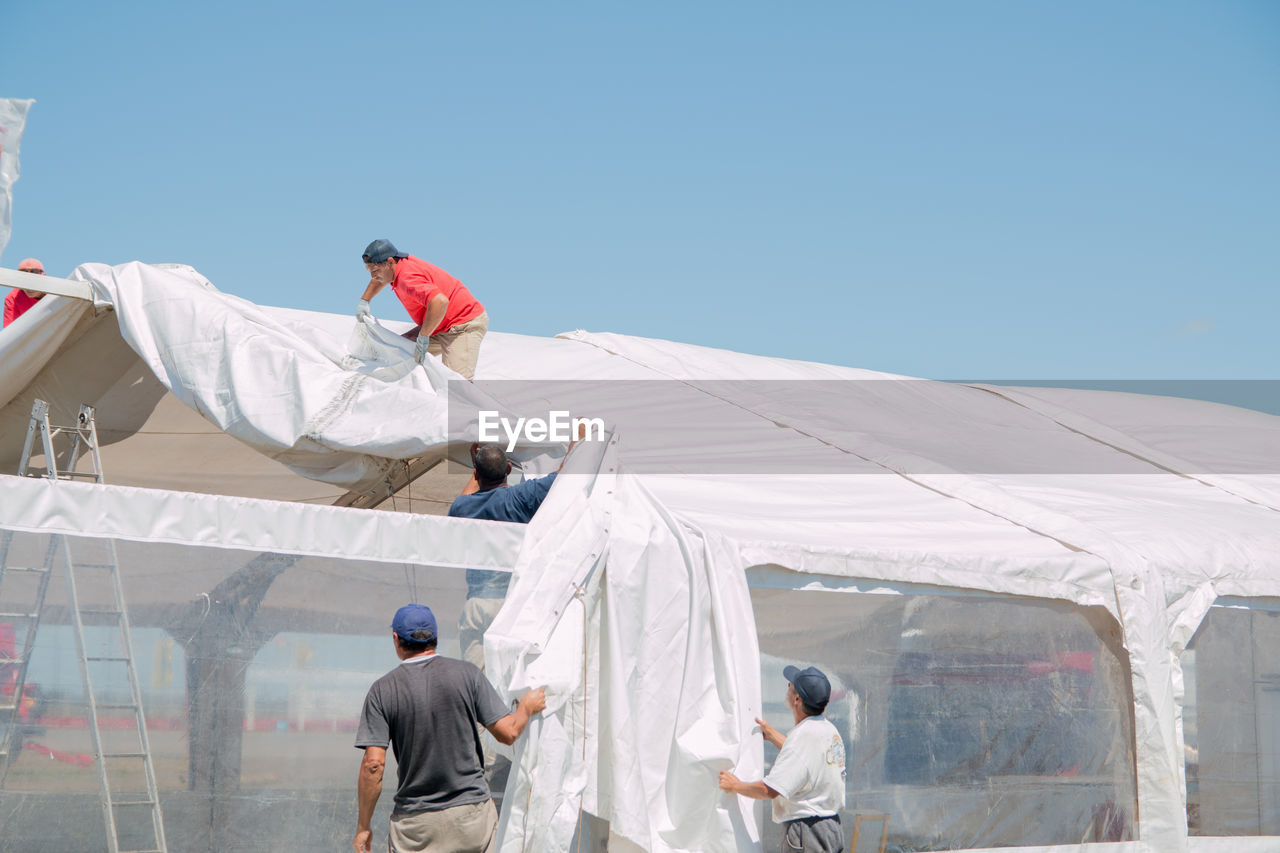 People covering greenhouse roof against clear sky