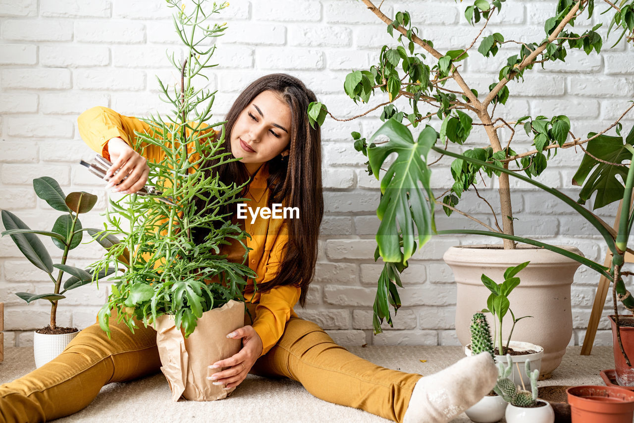 YOUNG WOMAN SITTING ON POTTED PLANT