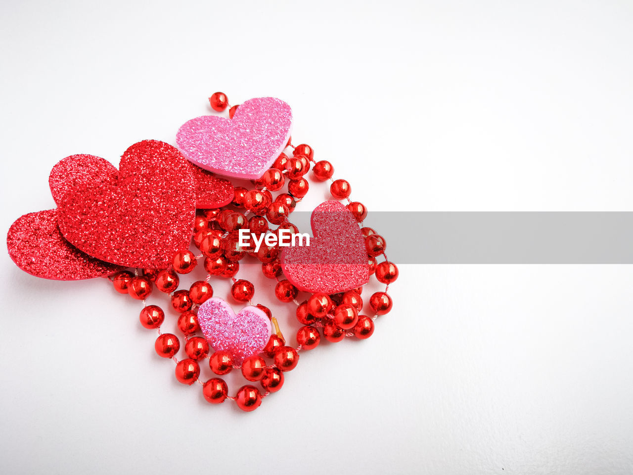 Close-up of heart shapes with red necklace over white background