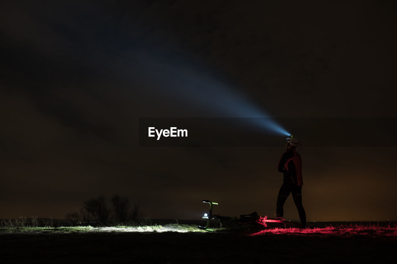 Man with headlamp standing on field against sky at night