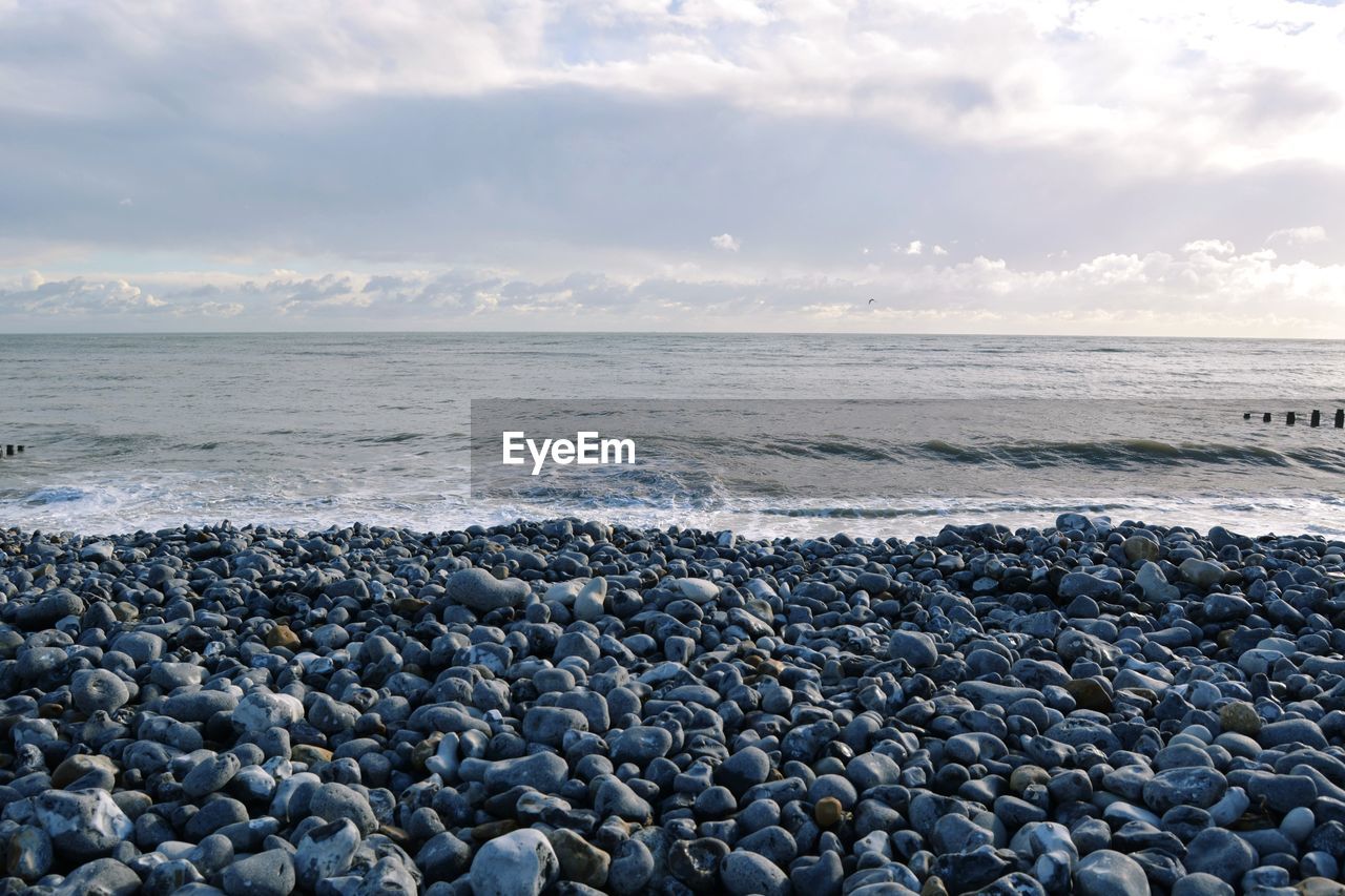 sea, water, beach, land, sky, shore, horizon, ocean, cloud, nature, beauty in nature, wave, horizon over water, pebble, rock, scenics - nature, wind wave, coast, body of water, tranquility, stone, environment, tranquil scene, sand, motion, travel destinations, seascape, landscape, no people, travel, breakwater, outdoors, coastline, water's edge, day, idyllic, tourism, dramatic sky, non-urban scene, holiday, trip, vacation, coastal feature, sunlight