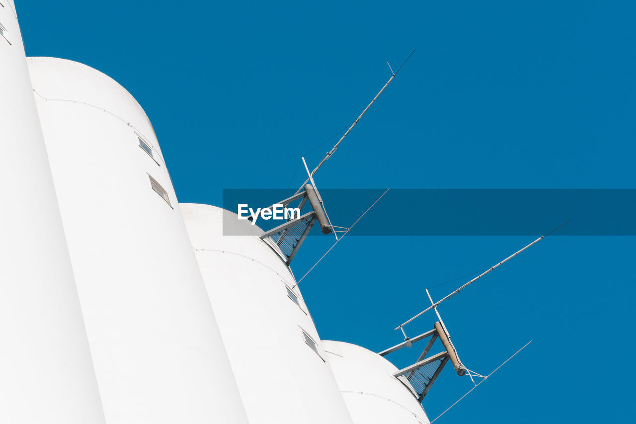 Low angle view of antennas on building against clear blue sky