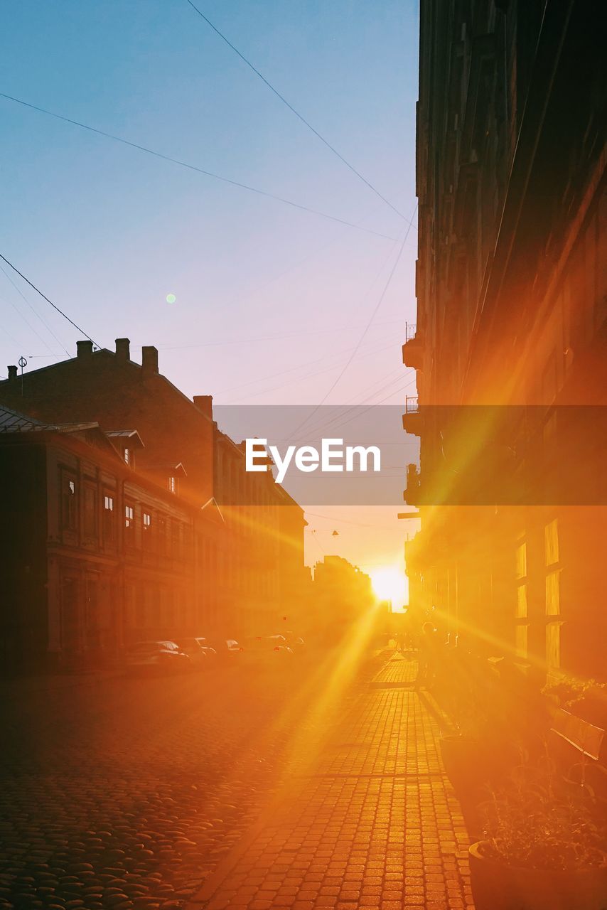 Street amidst buildings against sky during sunset