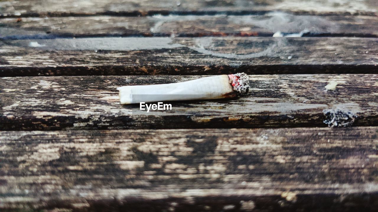 CLOSE-UP OF CIGARETTE SMOKING ON TABLE AGAINST WALL