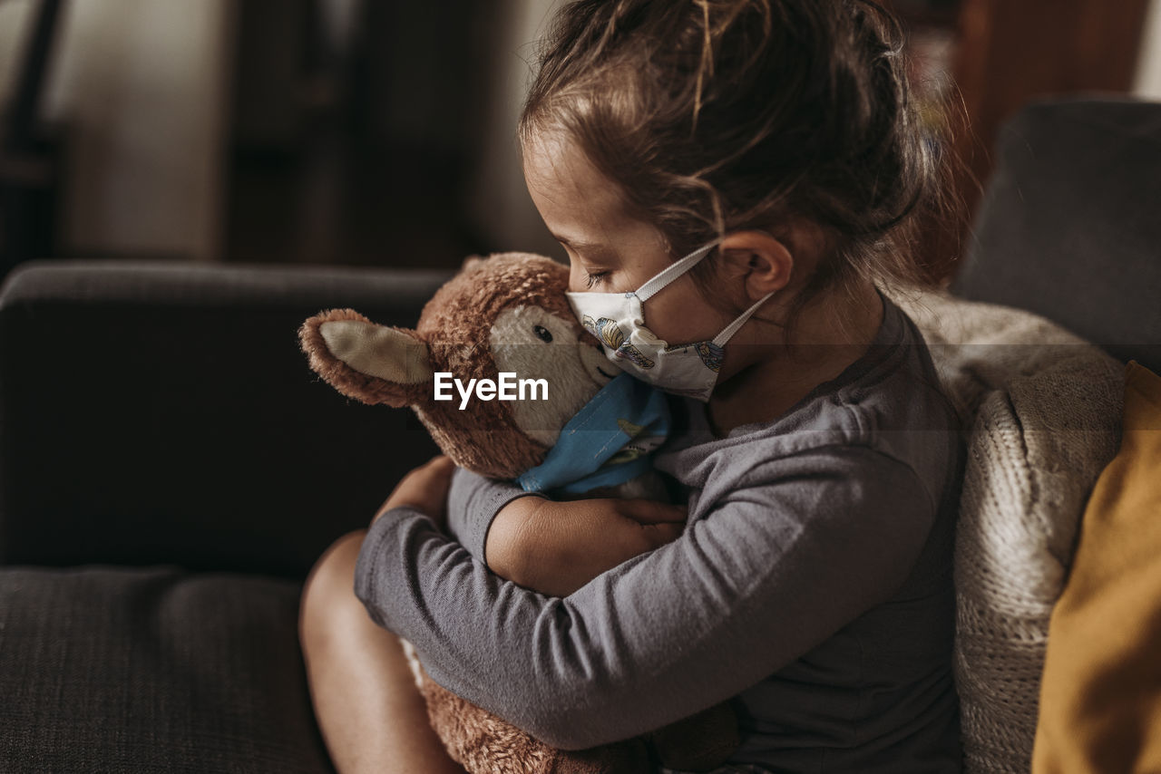 Close up of young girl with mask on kissing masked stuffed animal