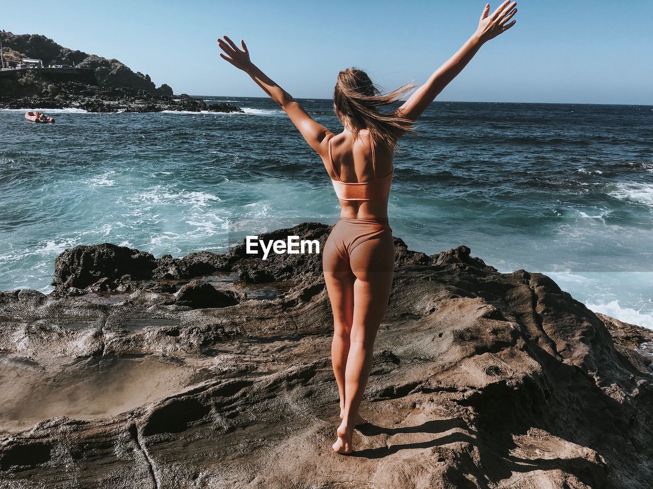 Rear view of woman standing in bikini on rocky shore