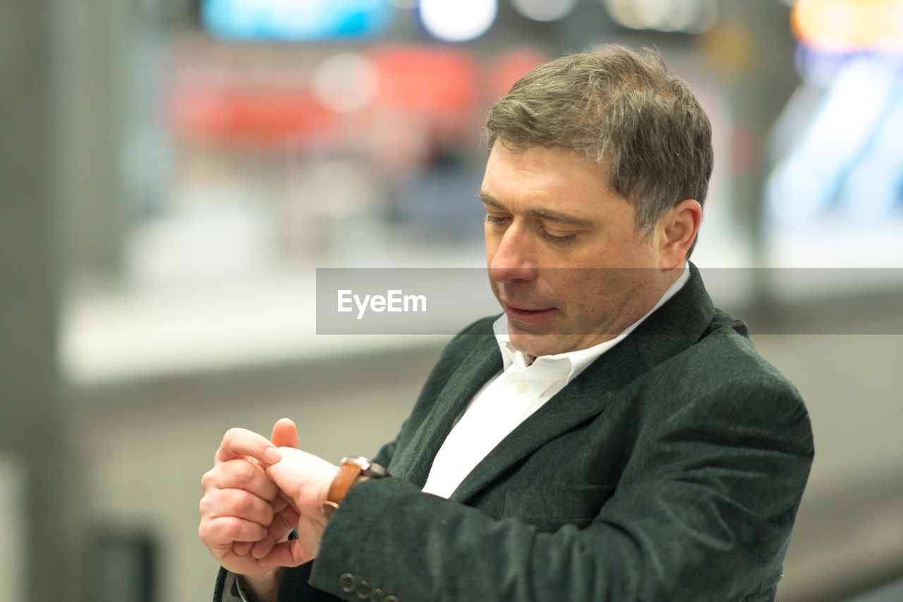 Thoughtful businessman checking time standing at railroad station platform