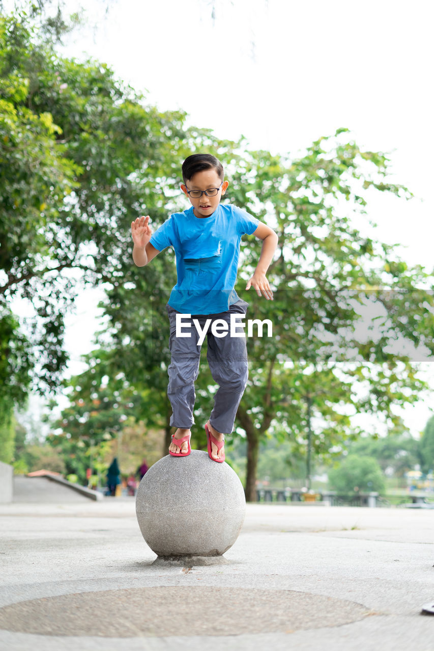 Outdoor portrait of a cute malaysian little boy trying to jump from a concrete ball at the park.