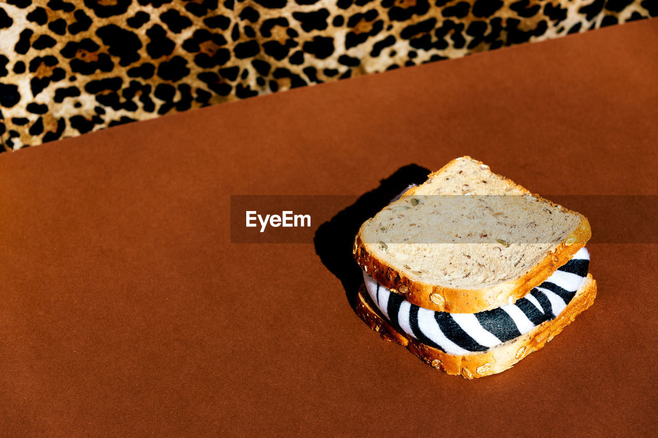 Crop anonymous person in shirt with leopard print sitting at brown table with sandwich with zebra filling in light room
