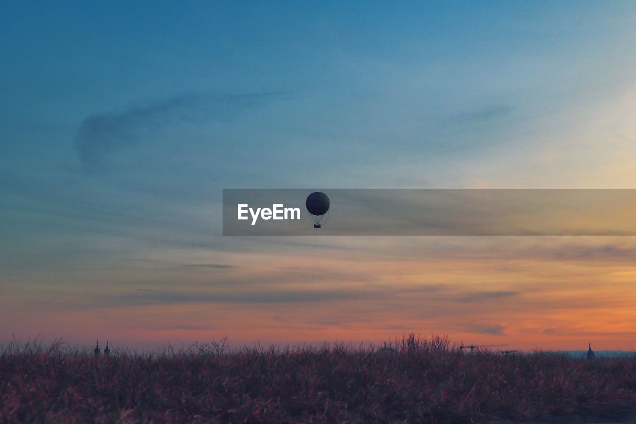 HOT AIR BALLOONS FLYING OVER FIELD DURING SUNSET