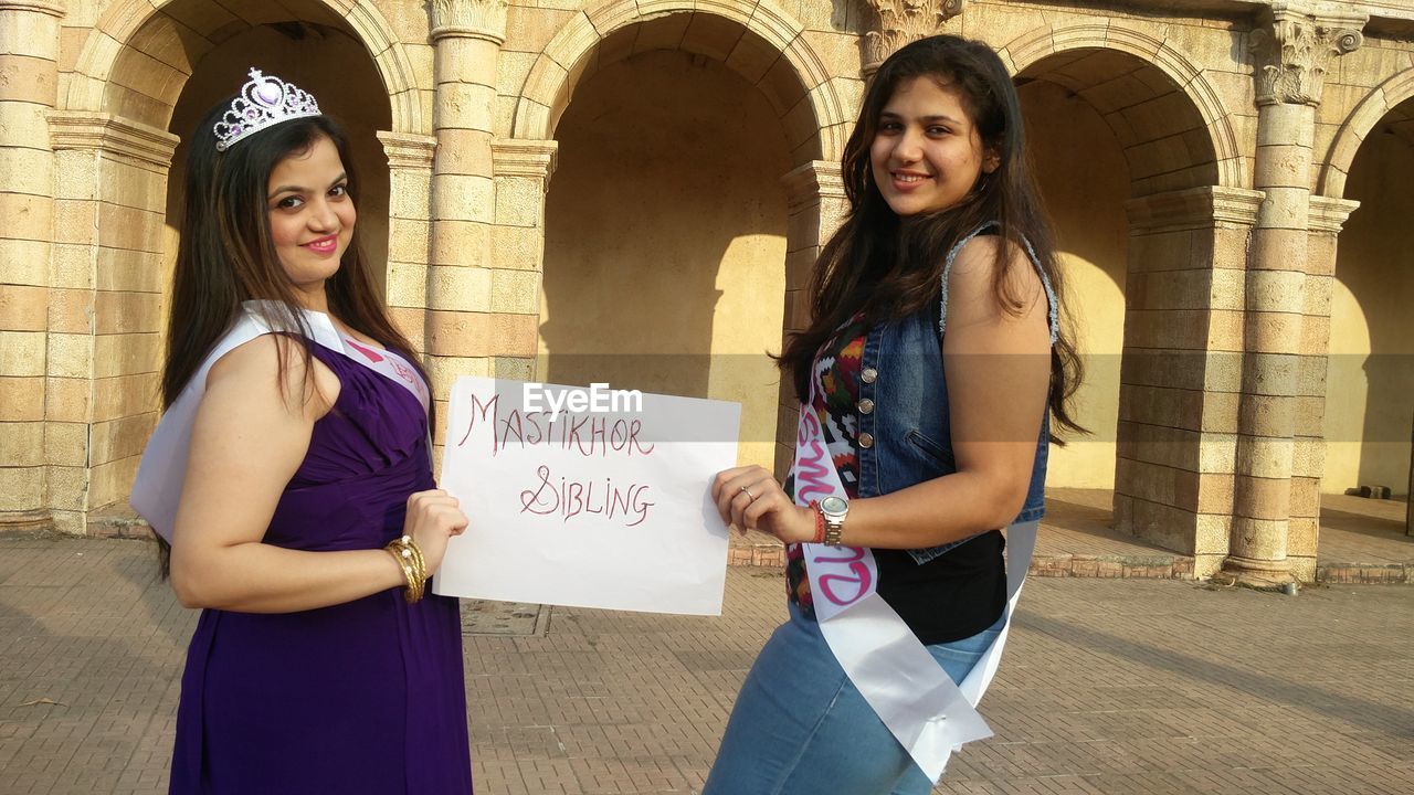 Portrait of smiling females showing placard while standing against building