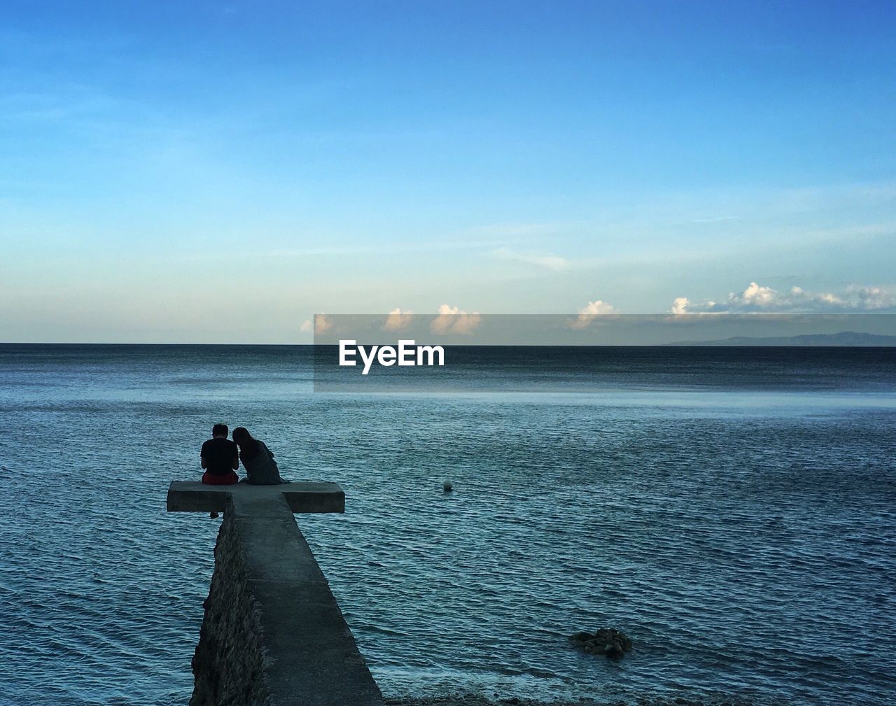 Rear view of couple sitting on pier against sea