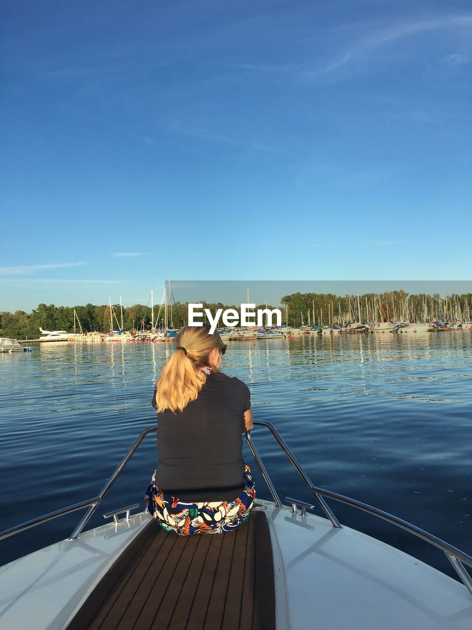 Rear view of mid adult woman sitting on boat in lake against blue sky