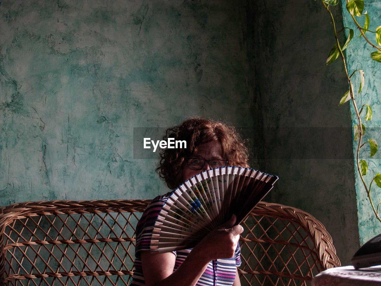 Portrait of woman covering face with hand fan at home