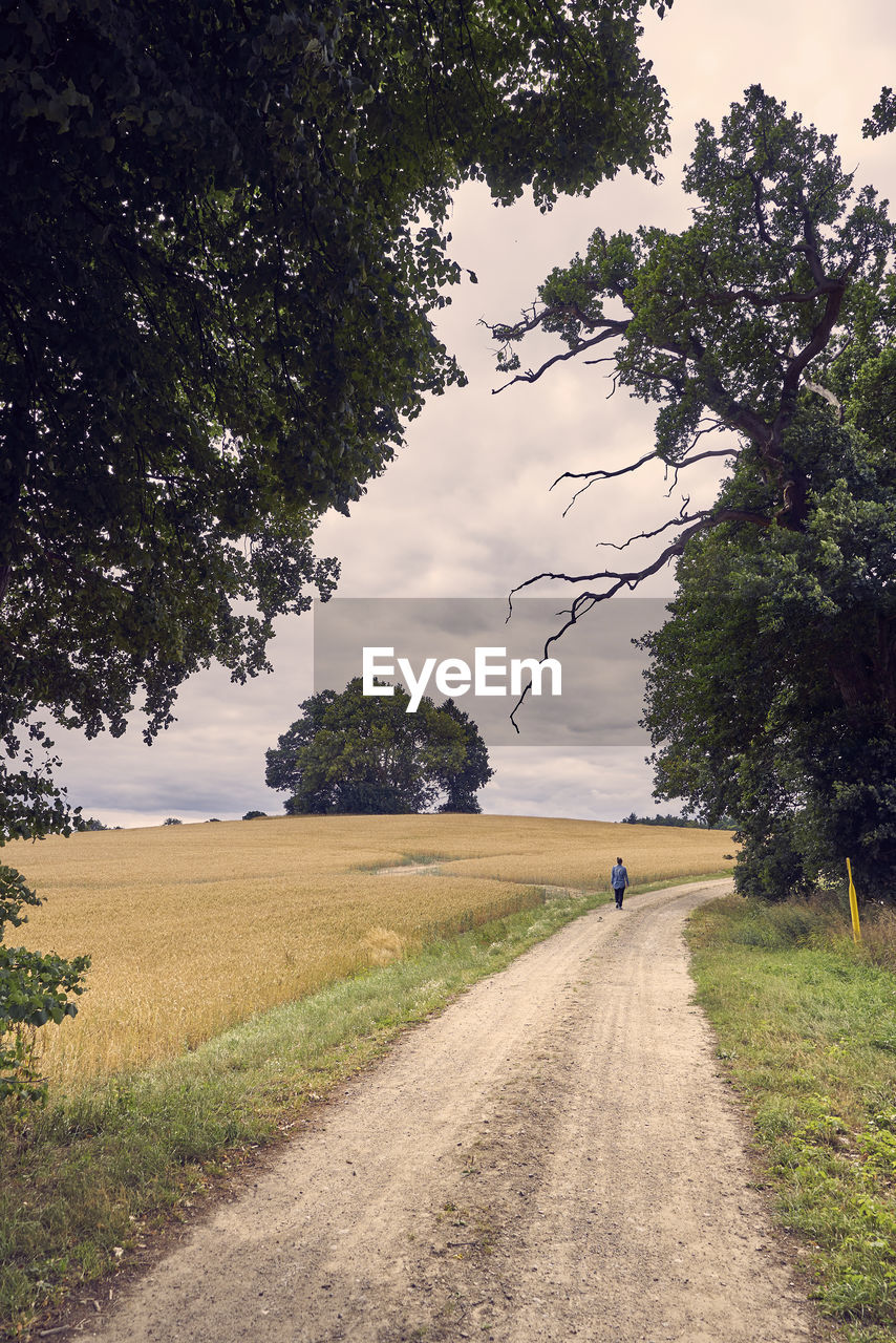 Dirt road amidst field against sky