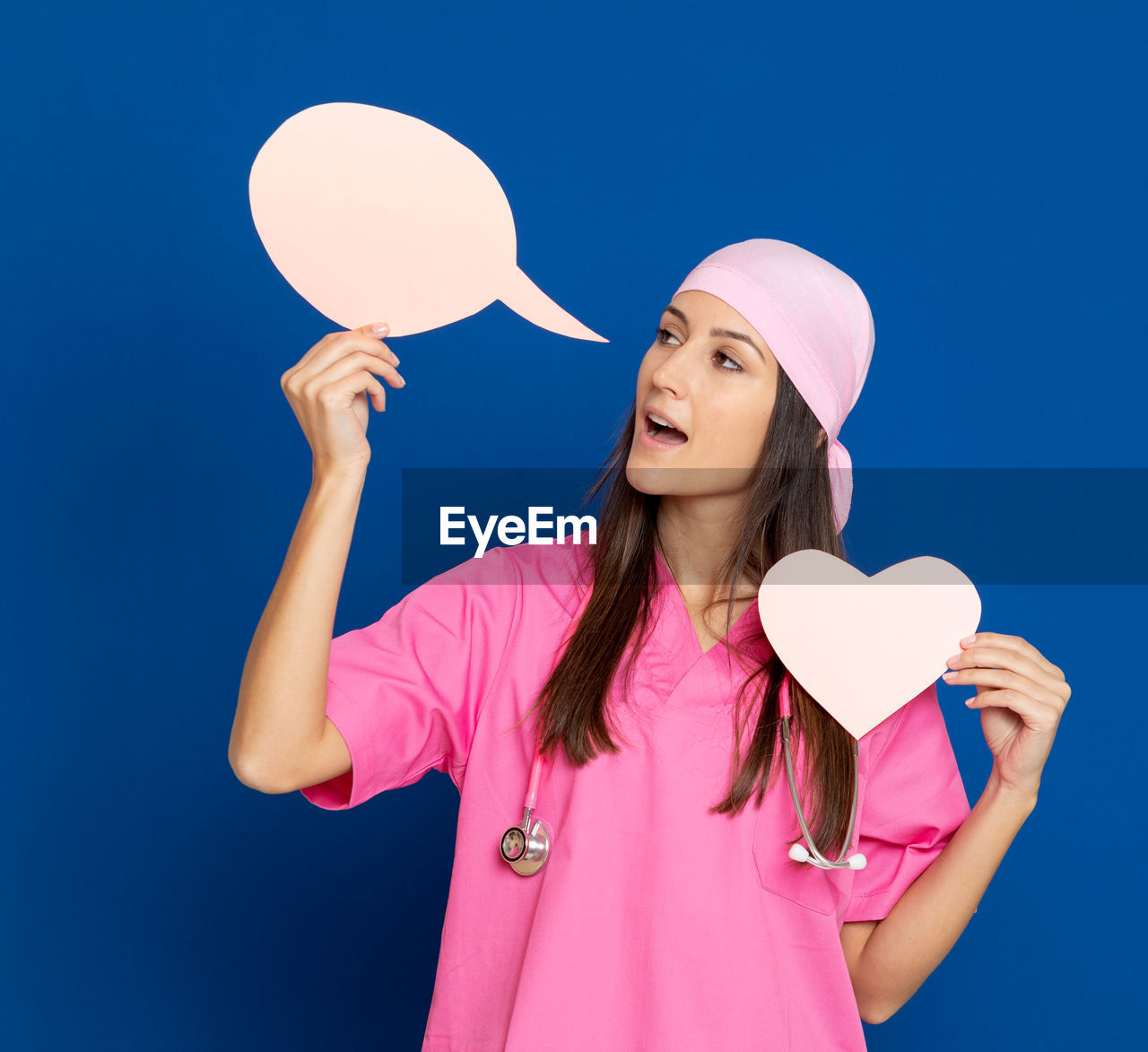 YOUNG WOMAN LOOKING AWAY WHILE STANDING ON PINK BALLOONS AGAINST BLUE SKY