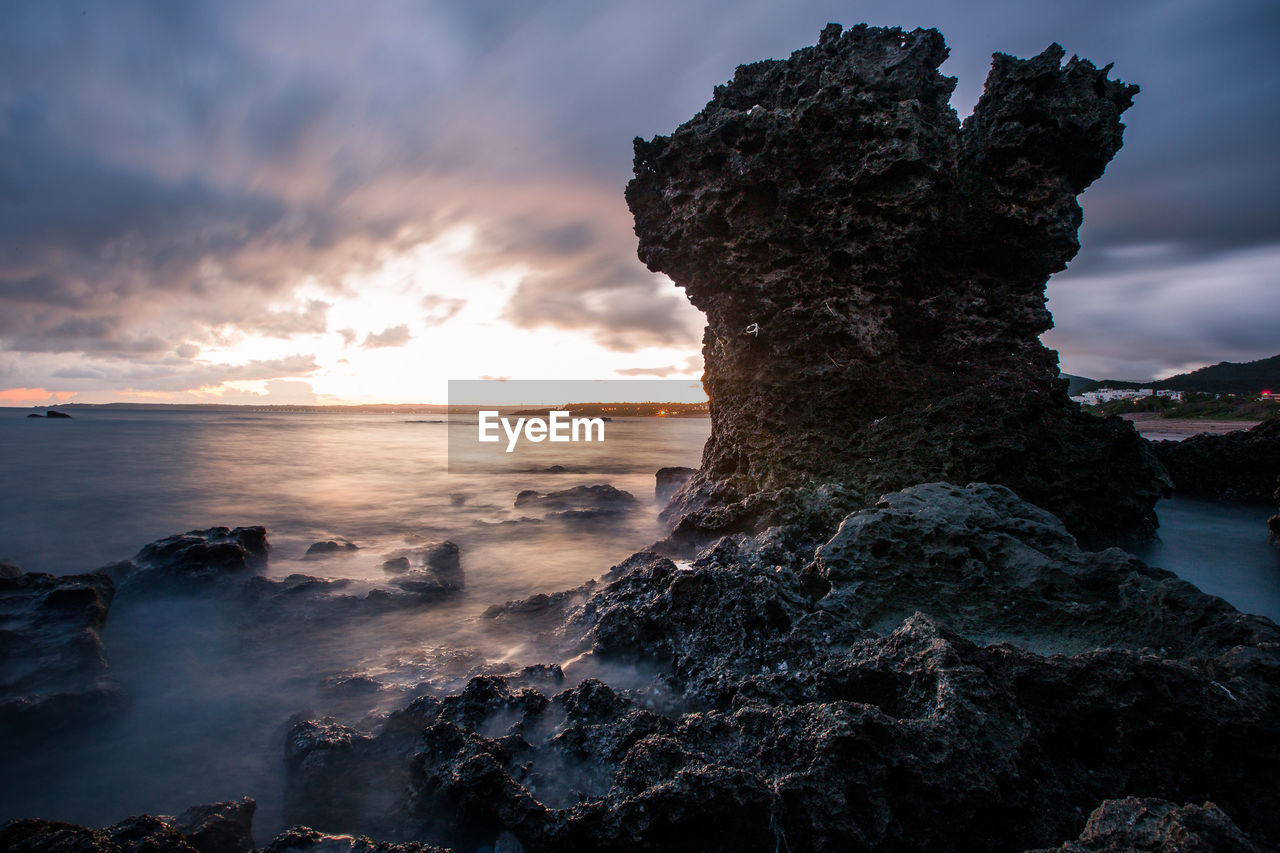 Rock formation on beach against sky during sunset