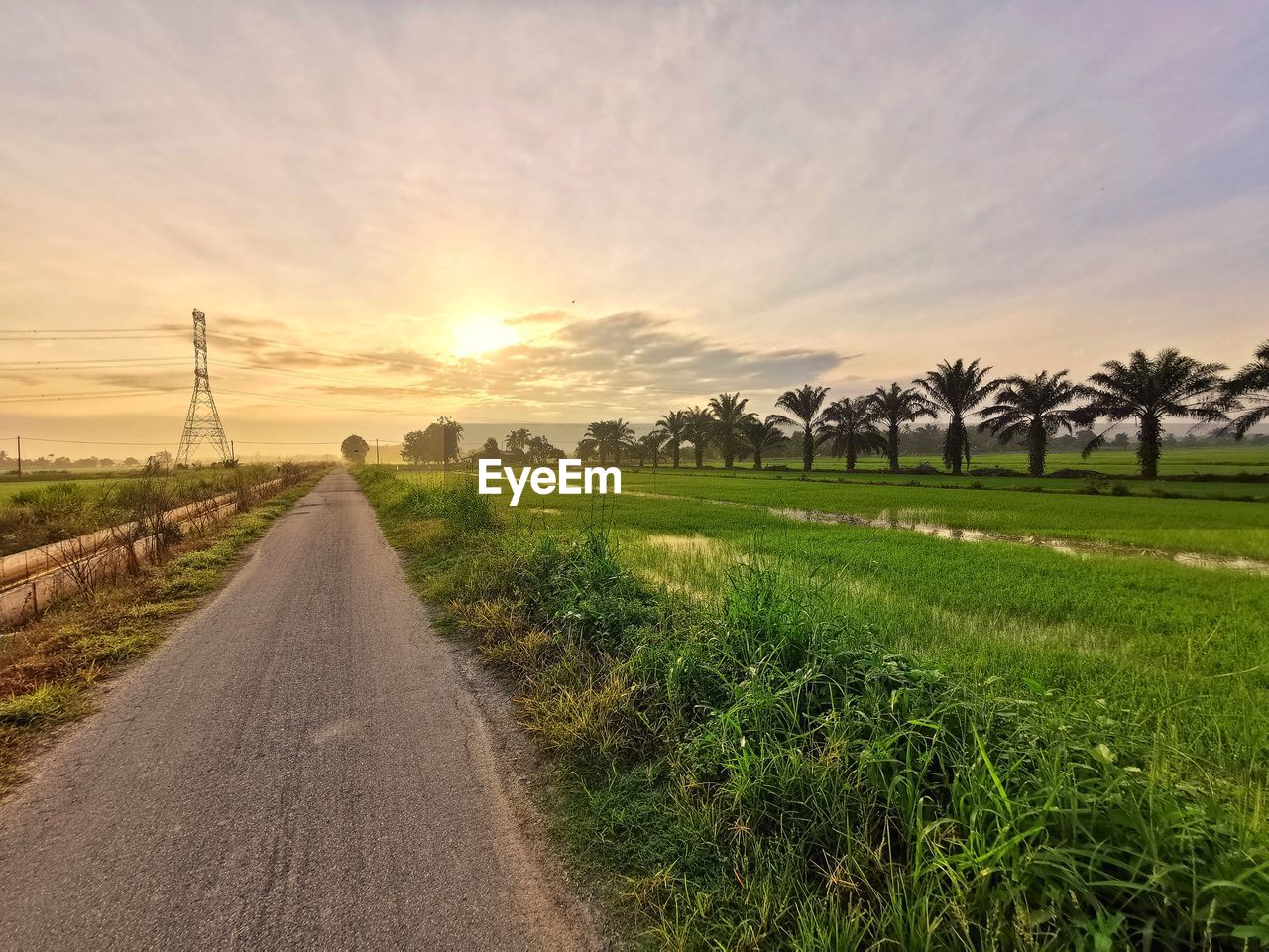 Road amidst field against sky during sunset