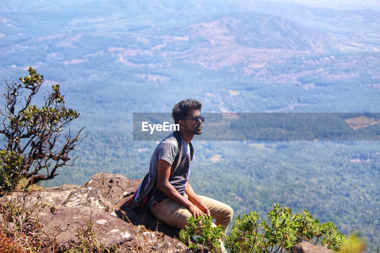 MAN SITTING ON ROCK LOOKING AT MOUNTAINS