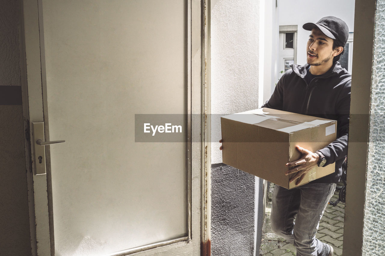 Confident delivery man with package standing at doorstep