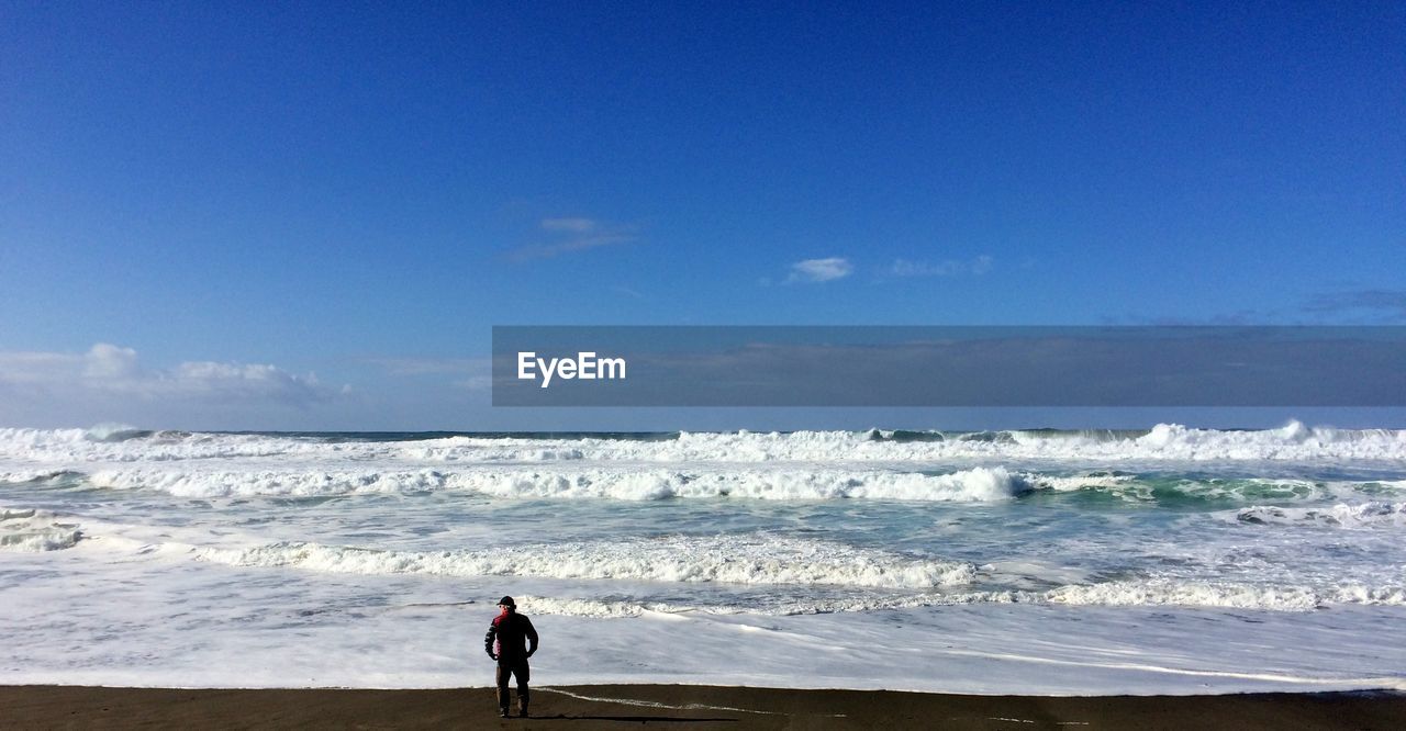 Rear view of a man on the beach contemplating the waves