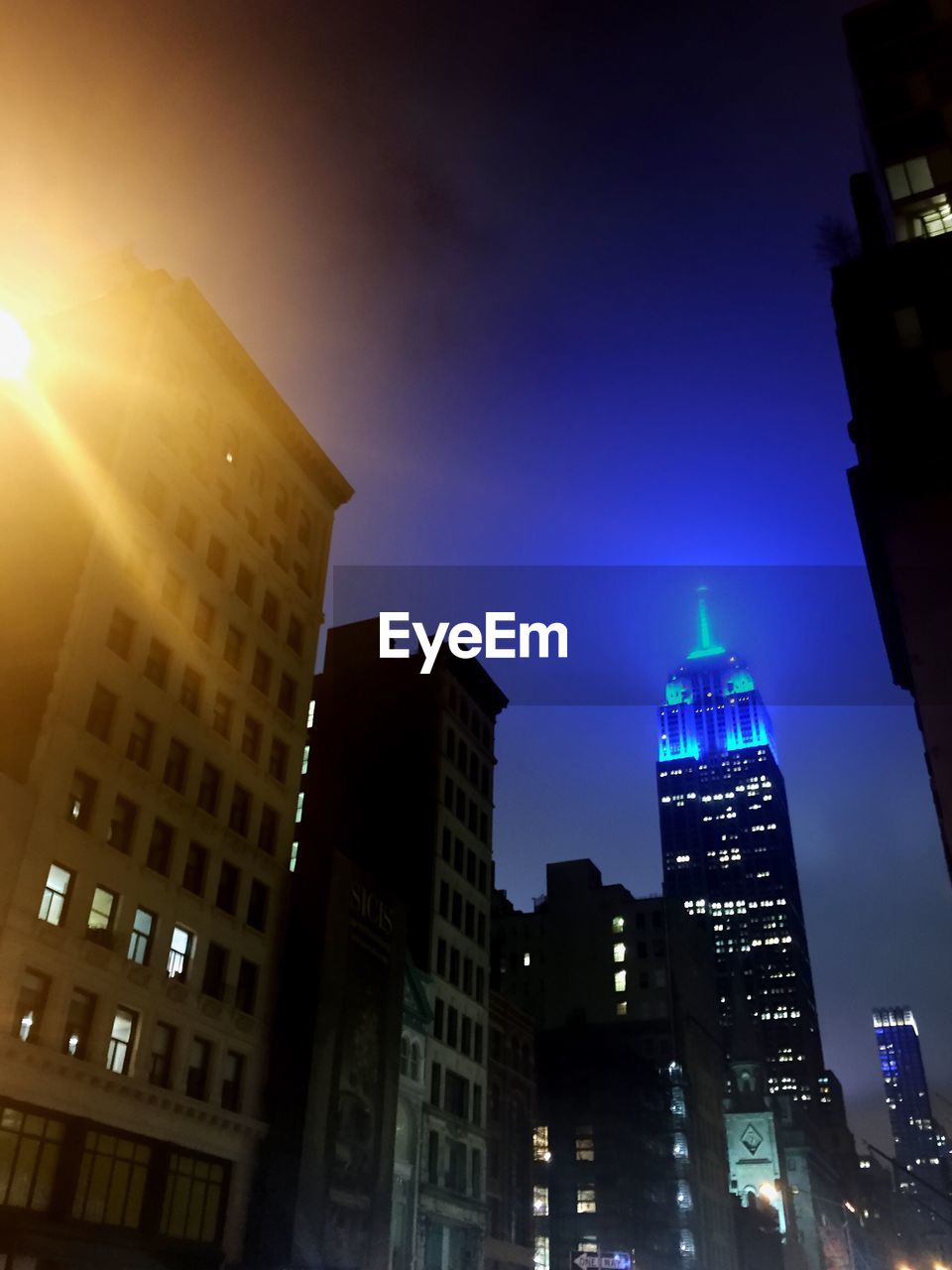 LOW ANGLE VIEW OF ILLUMINATED BUILDINGS AGAINST SKY AT NIGHT