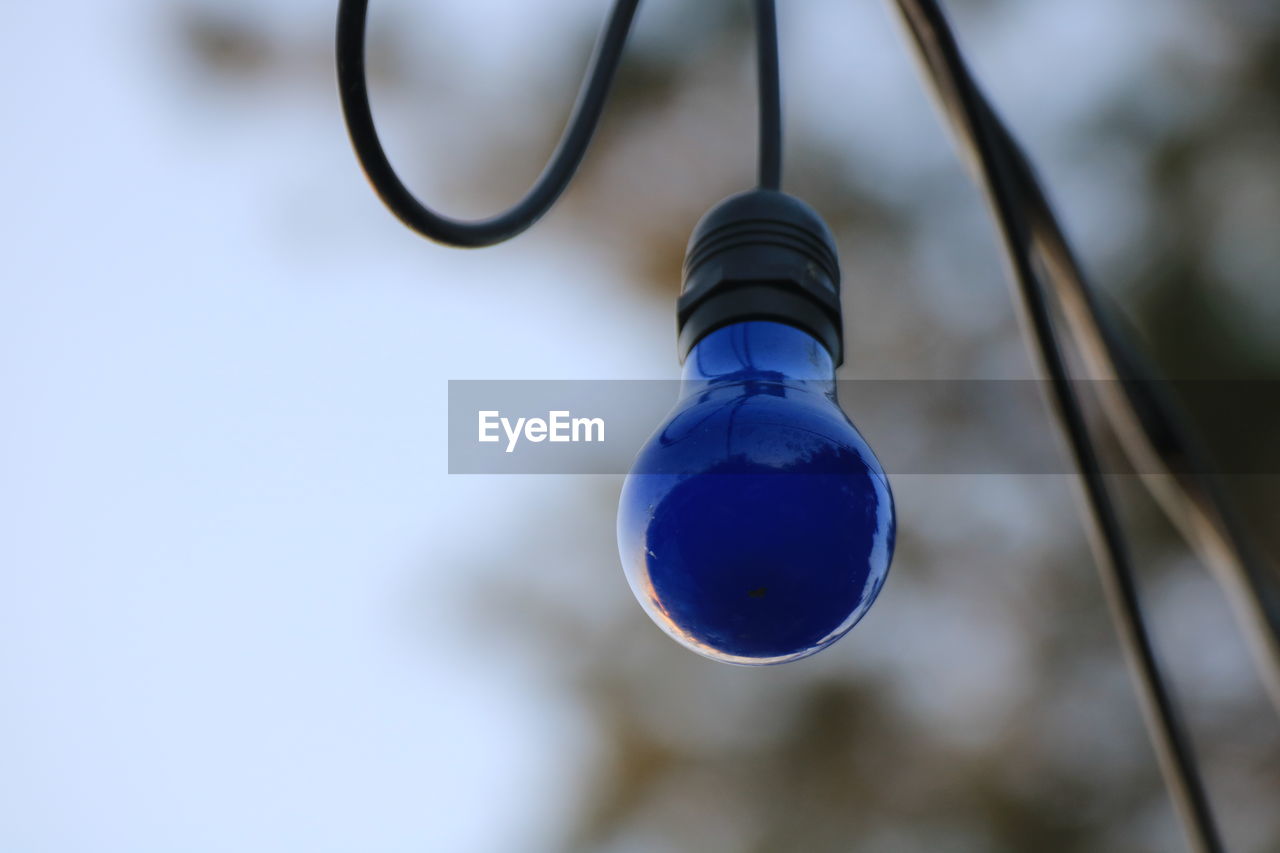 LOW ANGLE VIEW OF LIGHT BULB HANGING AGAINST BLURRED BACKGROUND